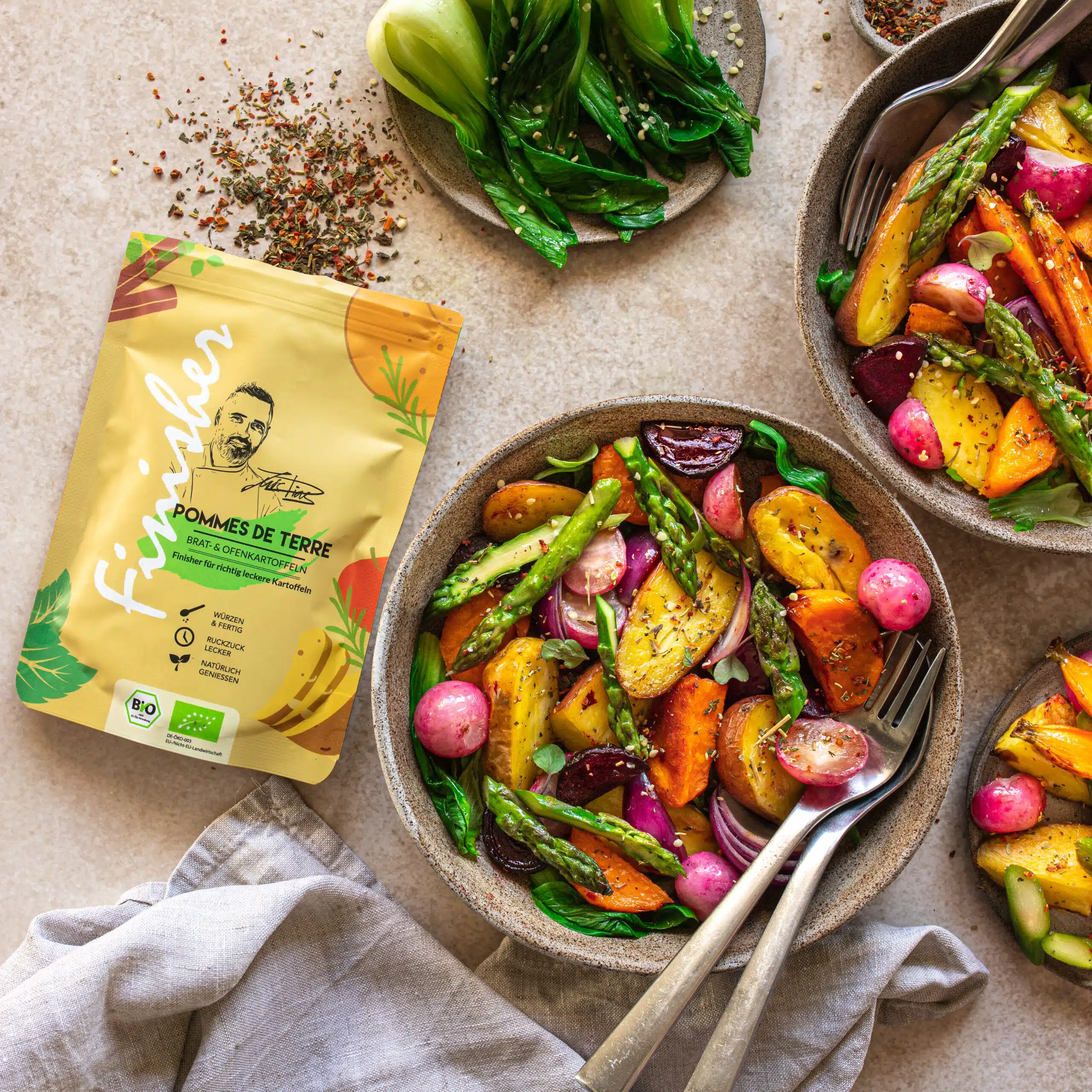 Die Gewürzpackung Pommes de Terre Finisher Spice liegt neben einem Teller mit einem Gemüsegericht aus Kartoffeln und Spargel