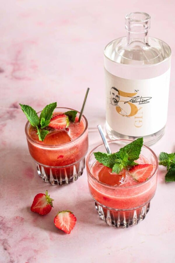 Das Foto zeigt Luis Dias Gin Flasche neben zwei Gin Tonic Gläsern mit Minze, umgeben von Erdbeeren