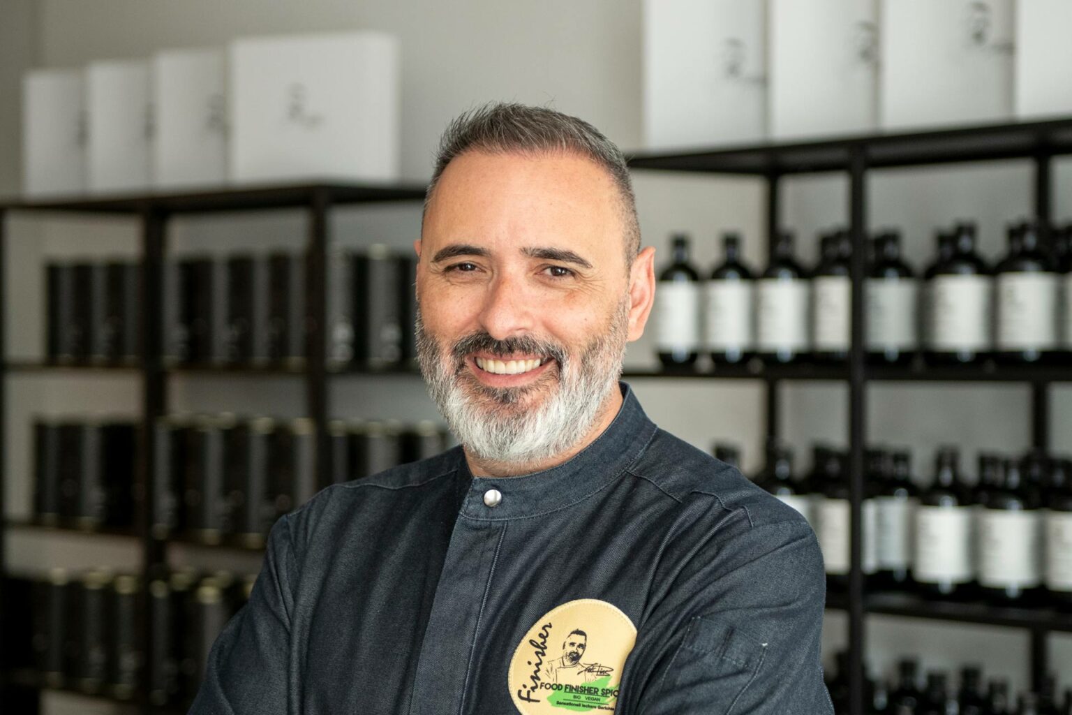 Luis Dias, der Inhaber von Casa Luis Dias, steht stolz vor zwei Regalen voller Gewürzpasten, Geschenkboxen und Olivenölen in seinem Laden.